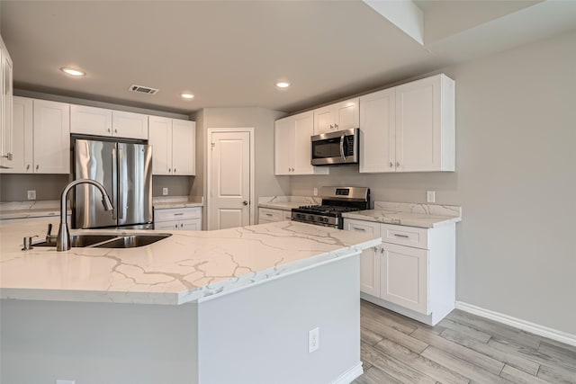 kitchen with sink, white cabinetry, light stone counters, stainless steel appliances, and light hardwood / wood-style floors