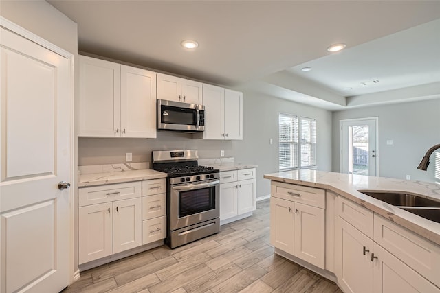 kitchen with appliances with stainless steel finishes, sink, white cabinets, light stone counters, and light wood-type flooring