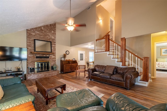 living room featuring ceiling fan, wood-type flooring, high vaulted ceiling, and a brick fireplace