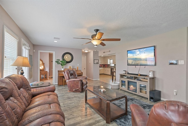 living room with ceiling fan, light hardwood / wood-style floors, and a textured ceiling