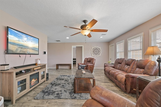 living room with ceiling fan, a textured ceiling, and light wood-type flooring