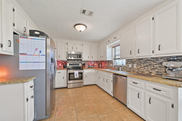 kitchen with appliances with stainless steel finishes, tasteful backsplash, sink, white cabinets, and light tile patterned floors