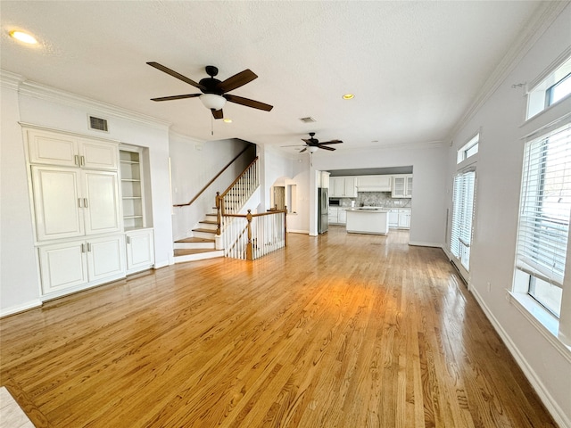 unfurnished living room featuring visible vents, crown molding, stairs, and light wood-style floors