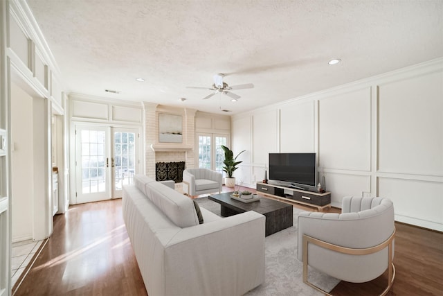 living room with a brick fireplace, light hardwood / wood-style flooring, ornamental molding, and a textured ceiling