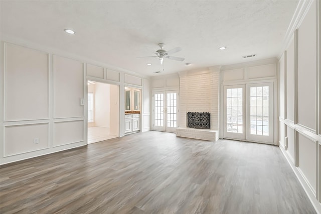 unfurnished living room with a brick fireplace, hardwood / wood-style flooring, french doors, and ceiling fan