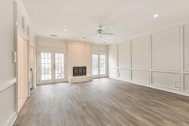 unfurnished living room featuring french doors, ornamental molding, hardwood / wood-style flooring, ceiling fan, and a fireplace