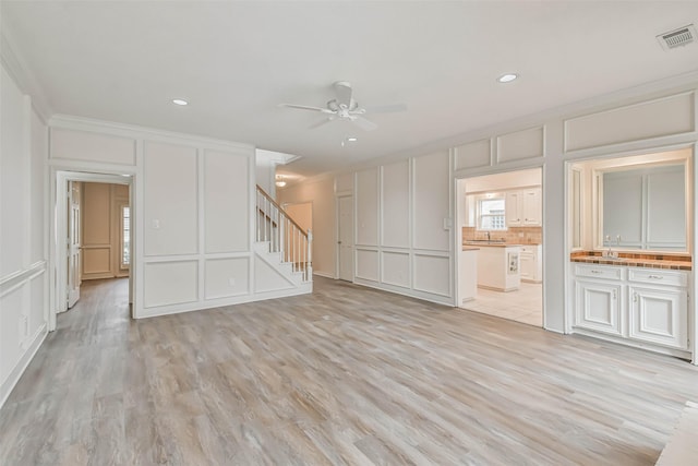 unfurnished living room with crown molding, ceiling fan, sink, and light wood-type flooring