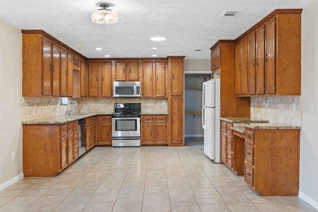 kitchen with light stone counters, sink, decorative backsplash, and stainless steel appliances