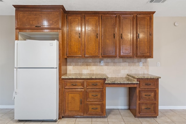 kitchen with tasteful backsplash, built in desk, light tile patterned floors, white refrigerator, and light stone countertops