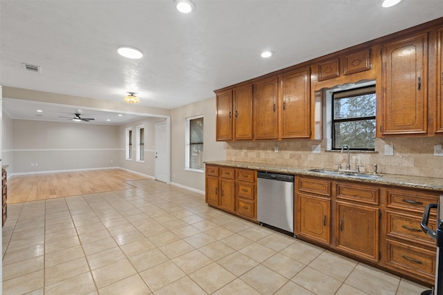 kitchen with light stone counters, stainless steel dishwasher, sink, and tasteful backsplash