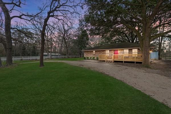 yard at dusk featuring dirt driveway, fence, and a wooden deck