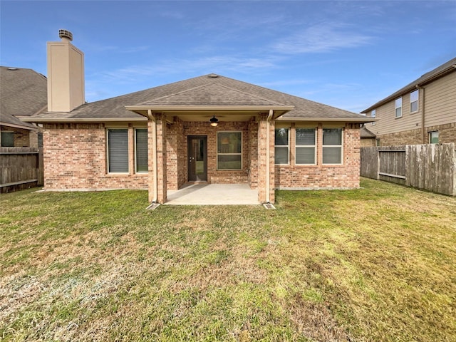 rear view of house with roof with shingles, brick siding, a lawn, a patio area, and a fenced backyard