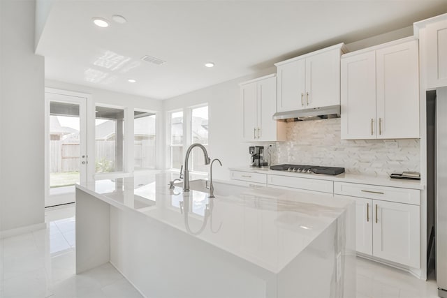 kitchen with tasteful backsplash, gas cooktop, an island with sink, and white cabinets