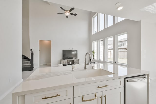 kitchen featuring a towering ceiling, dishwasher, white cabinetry, sink, and light stone countertops