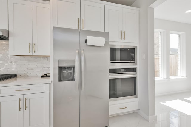 kitchen featuring white cabinetry, tasteful backsplash, appliances with stainless steel finishes, light stone countertops, and wall chimney range hood