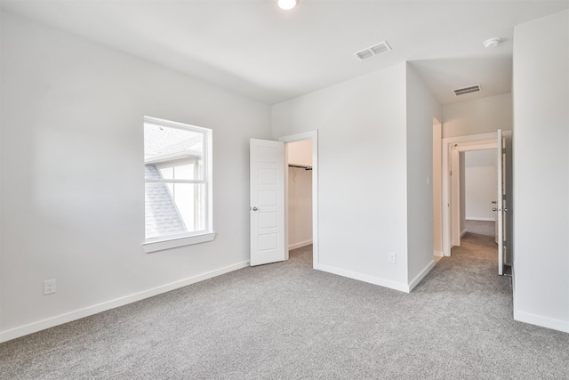 unfurnished bedroom featuring a walk in closet and light carpet