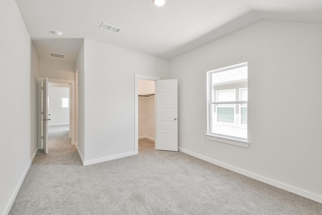 unfurnished bedroom featuring a closet, a walk in closet, vaulted ceiling, and light carpet