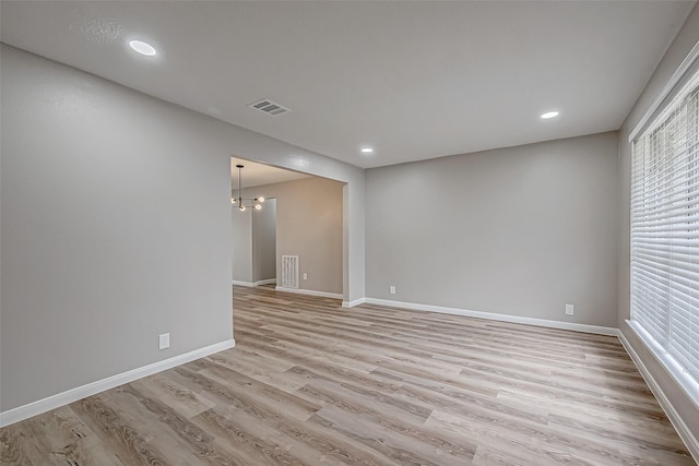 spare room featuring an inviting chandelier and light hardwood / wood-style flooring