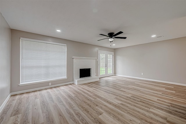 unfurnished living room with french doors, ceiling fan, a fireplace, and light hardwood / wood-style flooring