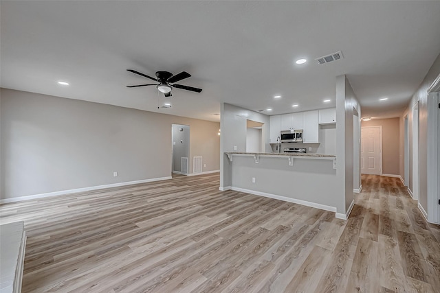 kitchen featuring light wood-type flooring, a kitchen breakfast bar, kitchen peninsula, ceiling fan, and white cabinets