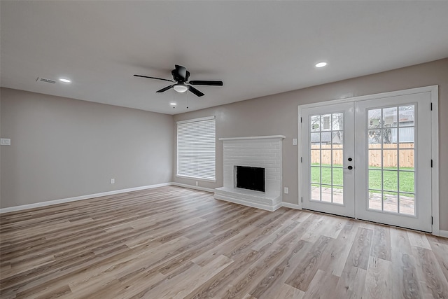 unfurnished living room with ceiling fan, a brick fireplace, light hardwood / wood-style floors, and french doors