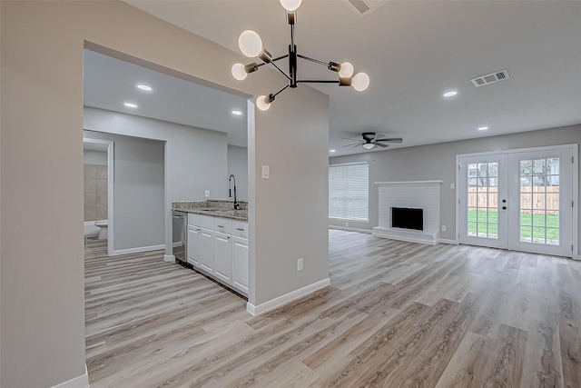 kitchen featuring sink, light stone counters, white cabinetry, a brick fireplace, and light hardwood / wood-style flooring