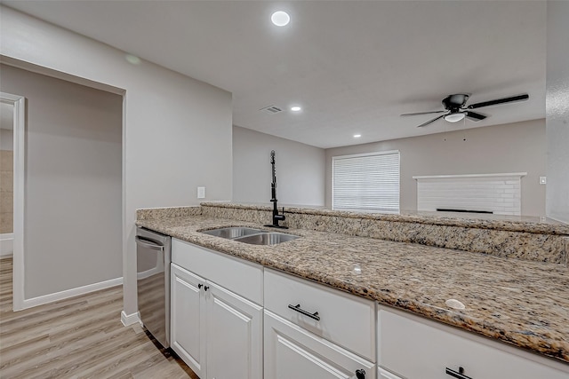 kitchen with sink, white cabinetry, a brick fireplace, dishwasher, and light stone countertops