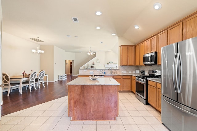 kitchen featuring sink, light tile patterned floors, stainless steel appliances, a kitchen island, and vaulted ceiling