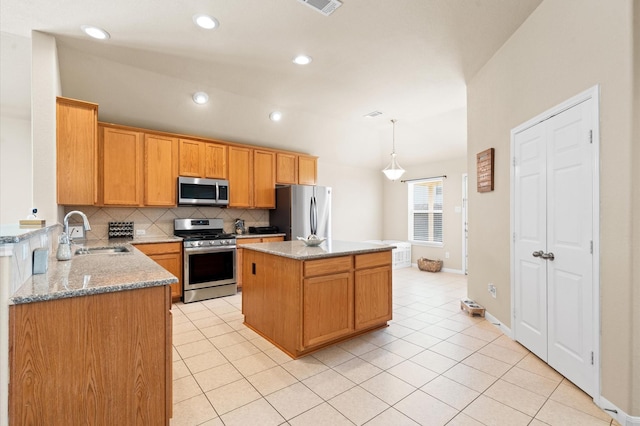 kitchen with sink, appliances with stainless steel finishes, light stone counters, a kitchen island, and decorative light fixtures