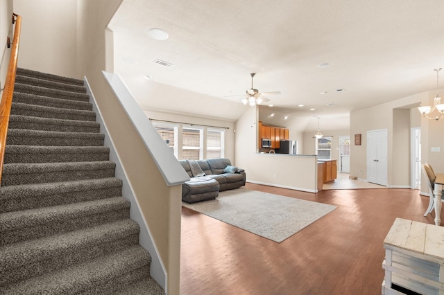 stairs with ceiling fan with notable chandelier, wood-type flooring, and vaulted ceiling