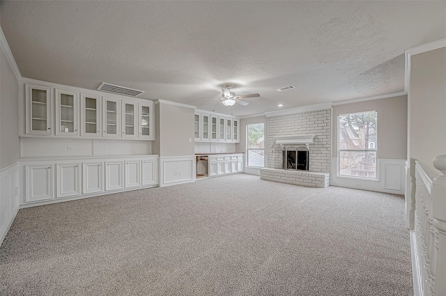 unfurnished living room featuring crown molding, a brick fireplace, light colored carpet, and ceiling fan