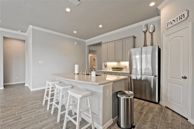 kitchen with a breakfast bar, gray cabinets, visible vents, freestanding refrigerator, and wood tiled floor