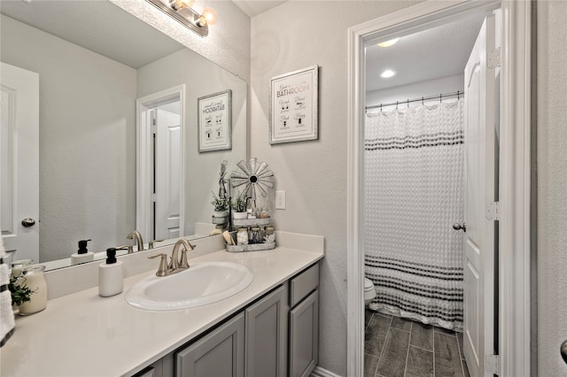 full bathroom featuring wood finish floors, a textured wall, vanity, and toilet