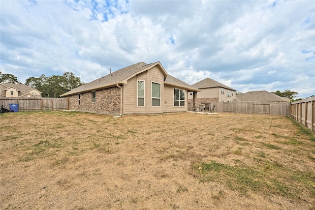 back of house with brick siding, a fenced backyard, a patio, and a yard