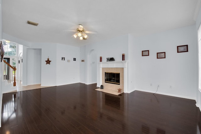 unfurnished living room with a tiled fireplace, dark wood-type flooring, and ceiling fan