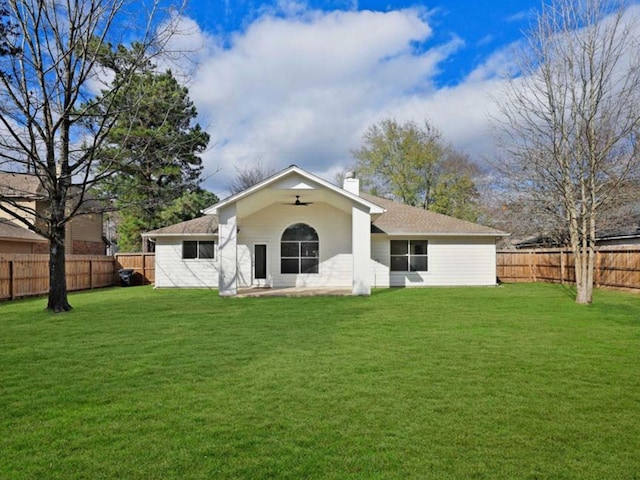 rear view of house with ceiling fan, a lawn, a chimney, and a fenced backyard