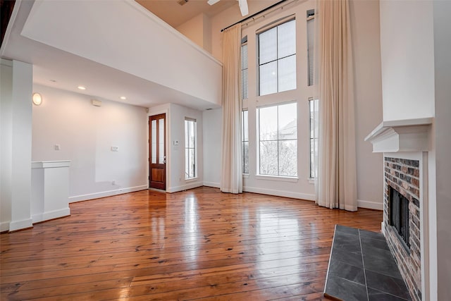 unfurnished living room featuring a high ceiling, a brick fireplace, wood finished floors, and baseboards