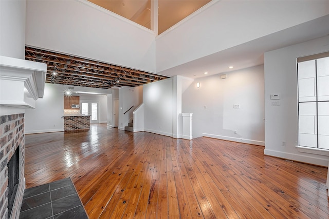 unfurnished living room featuring a brick fireplace, baseboards, stairway, and wood finished floors