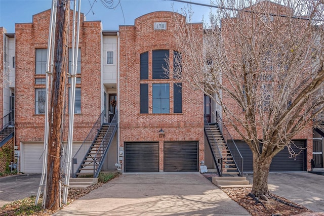 view of property with concrete driveway, brick siding, and stairs