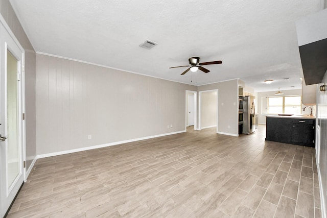 unfurnished living room featuring sink, light hardwood / wood-style flooring, a textured ceiling, ornamental molding, and ceiling fan