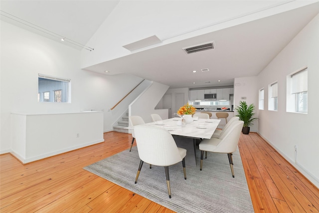 dining room featuring light wood-type flooring, stairway, visible vents, and vaulted ceiling