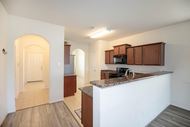 kitchen with light hardwood / wood-style flooring, black appliances, kitchen peninsula, and dark stone counters