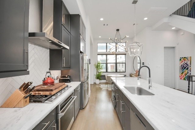 kitchen featuring sink, light stone counters, decorative light fixtures, wall chimney range hood, and stainless steel appliances