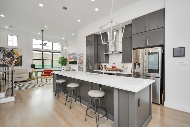 kitchen with a sink, decorative backsplash, appliances with stainless steel finishes, a kitchen bar, and wall chimney range hood