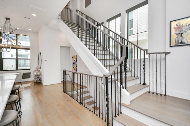 stairs featuring a high ceiling, hardwood / wood-style floors, and a notable chandelier