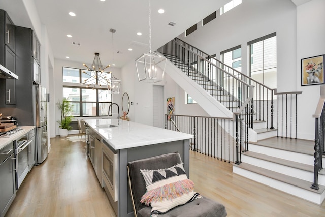 kitchen featuring a center island with sink, light wood-type flooring, pendant lighting, sink, and stainless steel fridge with ice dispenser