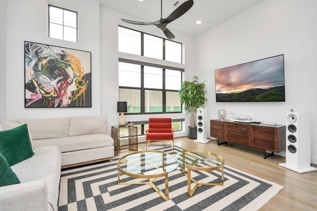 living room featuring plenty of natural light, ceiling fan, light hardwood / wood-style flooring, and a towering ceiling