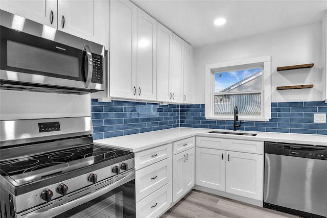 kitchen with stainless steel appliances, sink, white cabinets, and light hardwood / wood-style flooring