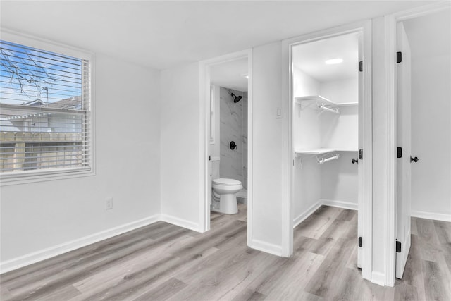 unfurnished bedroom with a closet, a walk in closet, connected bathroom, and light hardwood / wood-style flooring