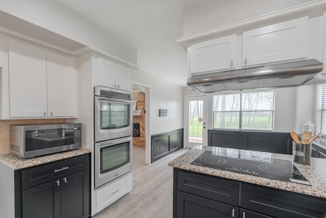 kitchen featuring appliances with stainless steel finishes, white cabinetry, backsplash, light stone countertops, and light wood-type flooring